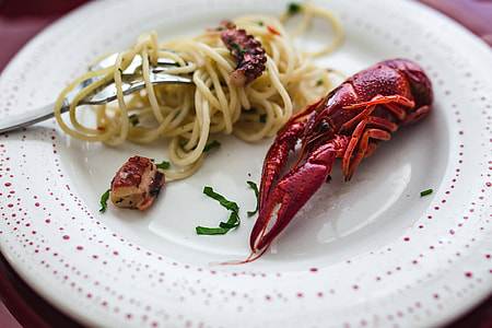 Fancy dinner with seafood pasta, crayfish and red wine by the table decorated with roses thumbnail