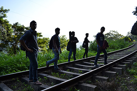 man walking along railroad track under blue sky thumbnail