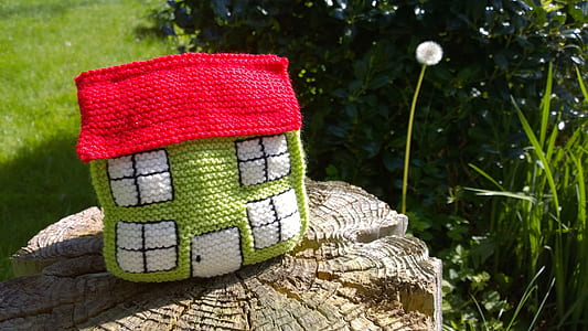 green and red knit miniature house on brown wood slab near green plants at daytime thumbnail
