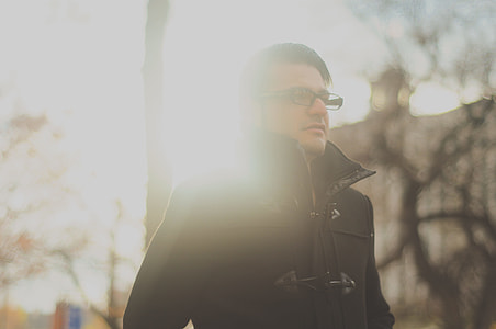 man wearing eyeglasses and duffel jacket near trees during day thumbnail
