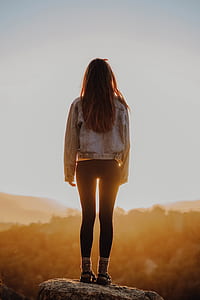 woman in blue denim jacket and black leggings standing next to mountains with yellow sunlight thumbnail