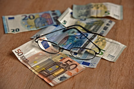 assorted euro banknotes and black frame eyeglasses on brown wooden surface thumbnail