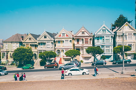 seven assorted-color uniform-shaped houses in front of street with lots of cars and several people during day thumbnail