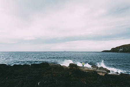 person standing on rock formation surrounded by body of water during daytime thumbnail