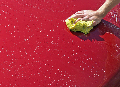 person holding yellow sponge cleaning red car thumbnail