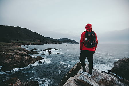 man standing on gray rocky mountain cliff overlooking sea during daytime thumbnail