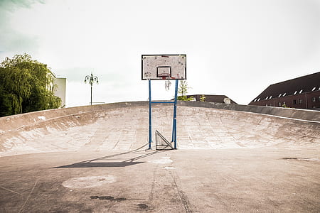 white and black basketball hoop system near green tree and brown building during daytime thumbnail
