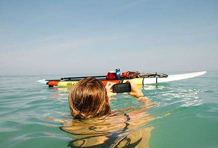 woman floating on body of water while taking photo of boat thumbnail