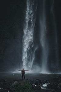man standing on waterfalls while spreading his arms thumbnail