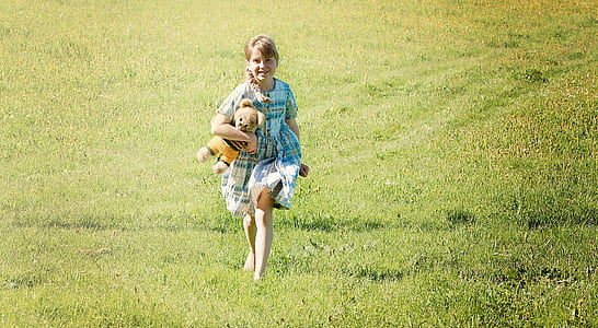 girl holding brown bear plush toy running on grass thumbnail