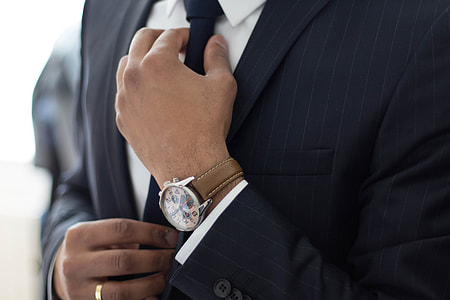 man in suit wearing watch holding necktie thumbnail