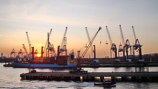 blue cargo ship docked near cranes during golden hour thumbnail