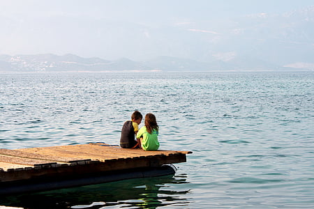 man and woman sitting on brown docking pier thumbnail