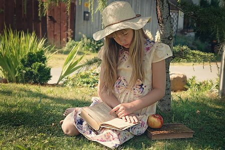 woman in yellow floral dress reading book under brown tree with brown sunhat beside red honeycrisp apple thumbnail
