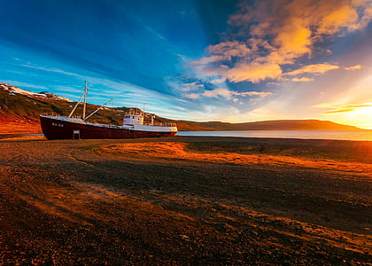 white and brown ship docked on seashore with mountain background thumbnail