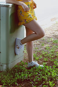 woman wearing yellow and multicolored floral miniskirt and white shoes leaning on gray metal garbage can thumbnail