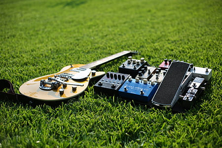 brown electric guitar and guitar effect pedals on grass field thumbnail