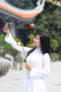 selective focus photography of woman wearing white turtle-neck long-sleeved shirt holding bray and brown bird and flower thumbnail