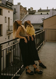 two women leaning on black railings while looking up thumbnail