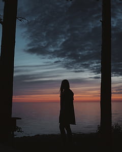 woman standing in front of body of water during sunset thumbnail