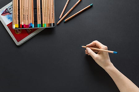 person holding color pencil on black panel thumbnail