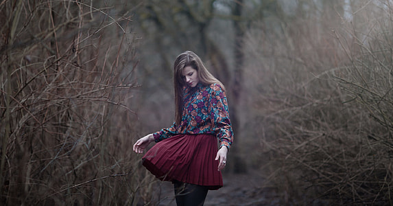 woman looking at her skirt standing between brown twigs outdoors thumbnail