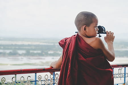boy wearing red traditional dress standing in front of body of water thumbnail