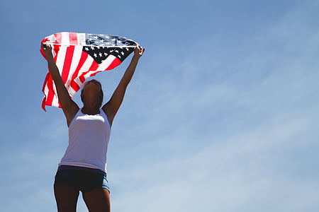 standing woman holding waving USA flag during daytime thumbnail