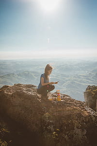 woman using smartphone squating on brown rock in aerial photography thumbnail