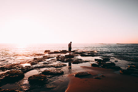 person standing on rock white looking on body of water thumbnail