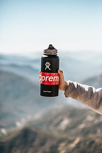 person holding black and red Supreme tumbler during daytime thumbnail