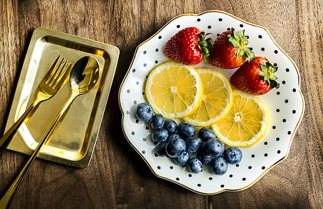three red strawberries, blueberries and sliced lemons on white plate thumbnail