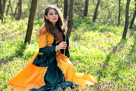 woman in orange and green long-sleeved dress sitting in the woods during daytime thumbnail