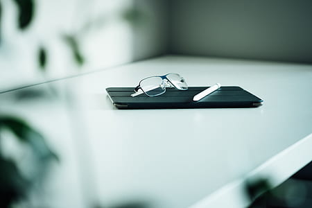 Apple Pen and black framed eyeglasses on top of tablet with black flip case thumbnail