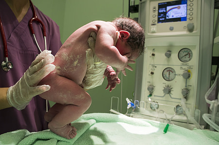 person wearing purple scrub top holding new born baby thumbnail