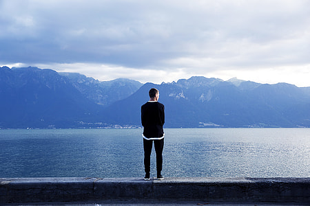 man standing on ledge near body of water thumbnail