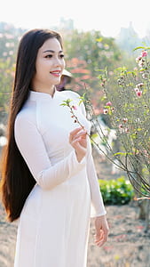 woman wearing white long-sleeved dress near pink petaled flower plant thumbnail