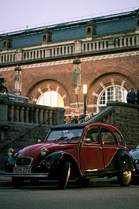 red and black Volkswagen Beetle parked beside brown building thumbnail