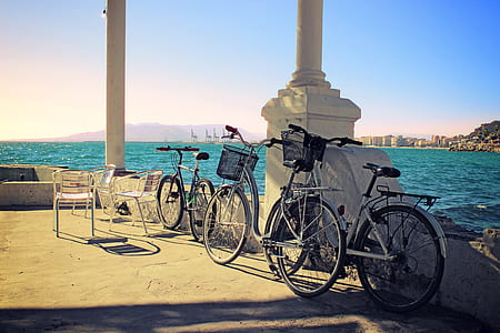three bicycles parked upright on pillar near body of water during daytime thumbnail