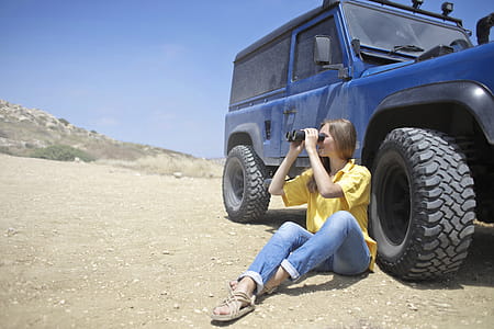 Woman Sitting on Soil Beside Jeep While Using Binoculars thumbnail