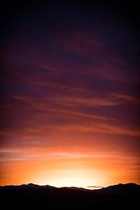 silhouette photography of mountains under cloudy skies during golden hour thumbnail
