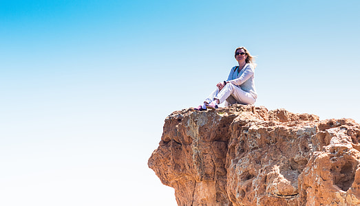 woman sitting on top of brown rock cliff under blue sky at daytime thumbnail