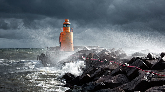 rough waves splashing through orange lighthouse photo thumbnail