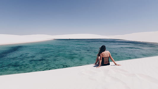 woman wearing black swimsuit sitting on white sand beach thumbnail