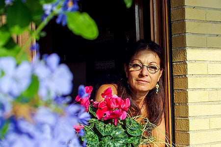 woman in window near red Geranium flower thumbnail