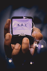 person holding opened Kay Jeweler engagement ring box with string lights thumbnail