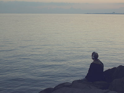man sitting on rocks near body of water thumbnail