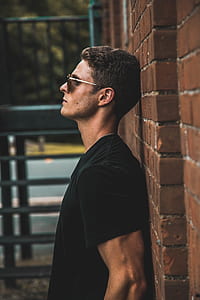 man wearing black crew-neck shirt leaning on brick wall during day time thumbnail