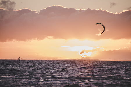 person paragliding on body of water under cloudy sky at golden hour thumbnail