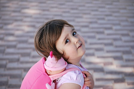 girl in pink cap-sleeved shirt carrying backpack with baby doll thumbnail